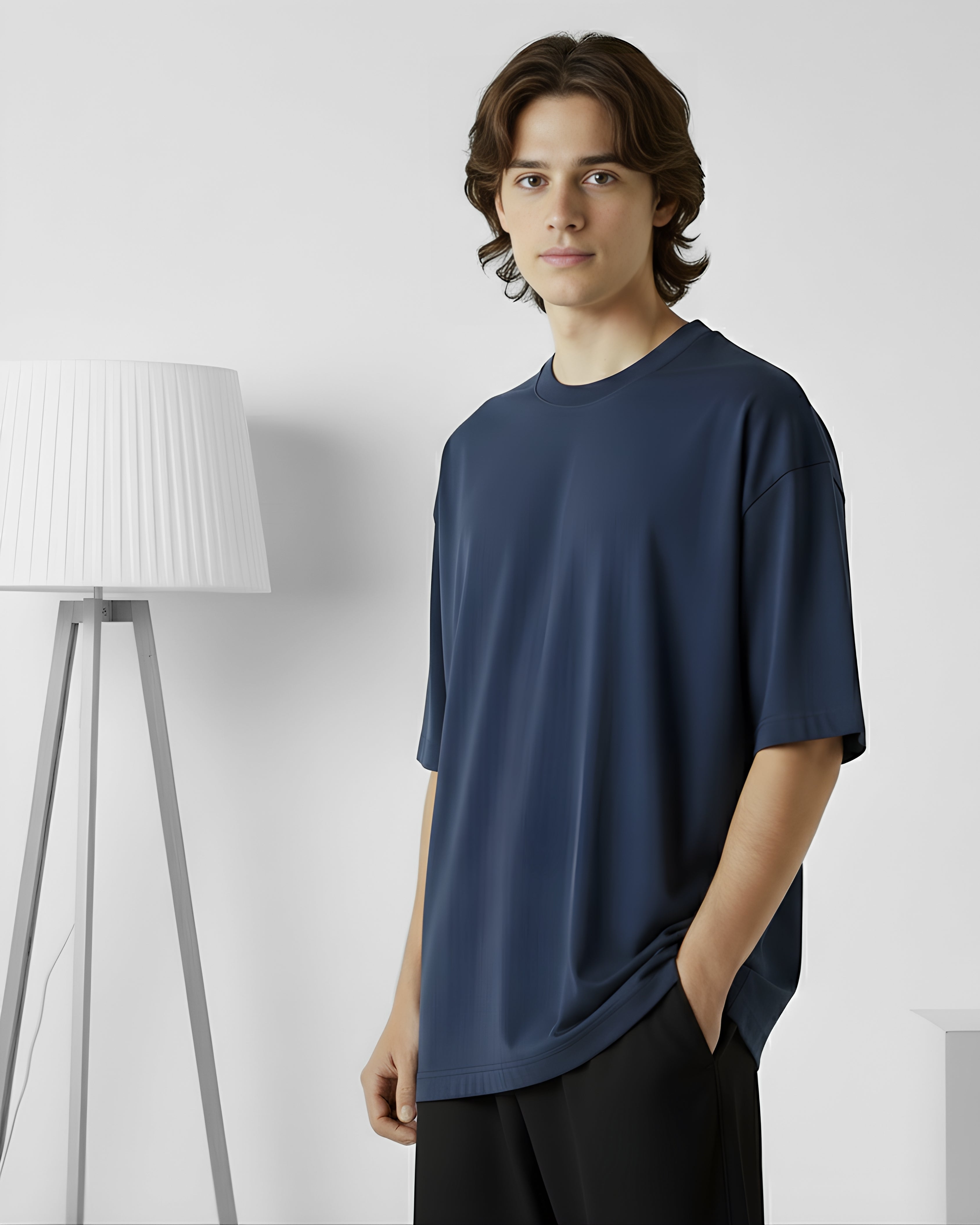 Man wearing a navy blue t-shirt standing in a minimalistic room with a white lamp.