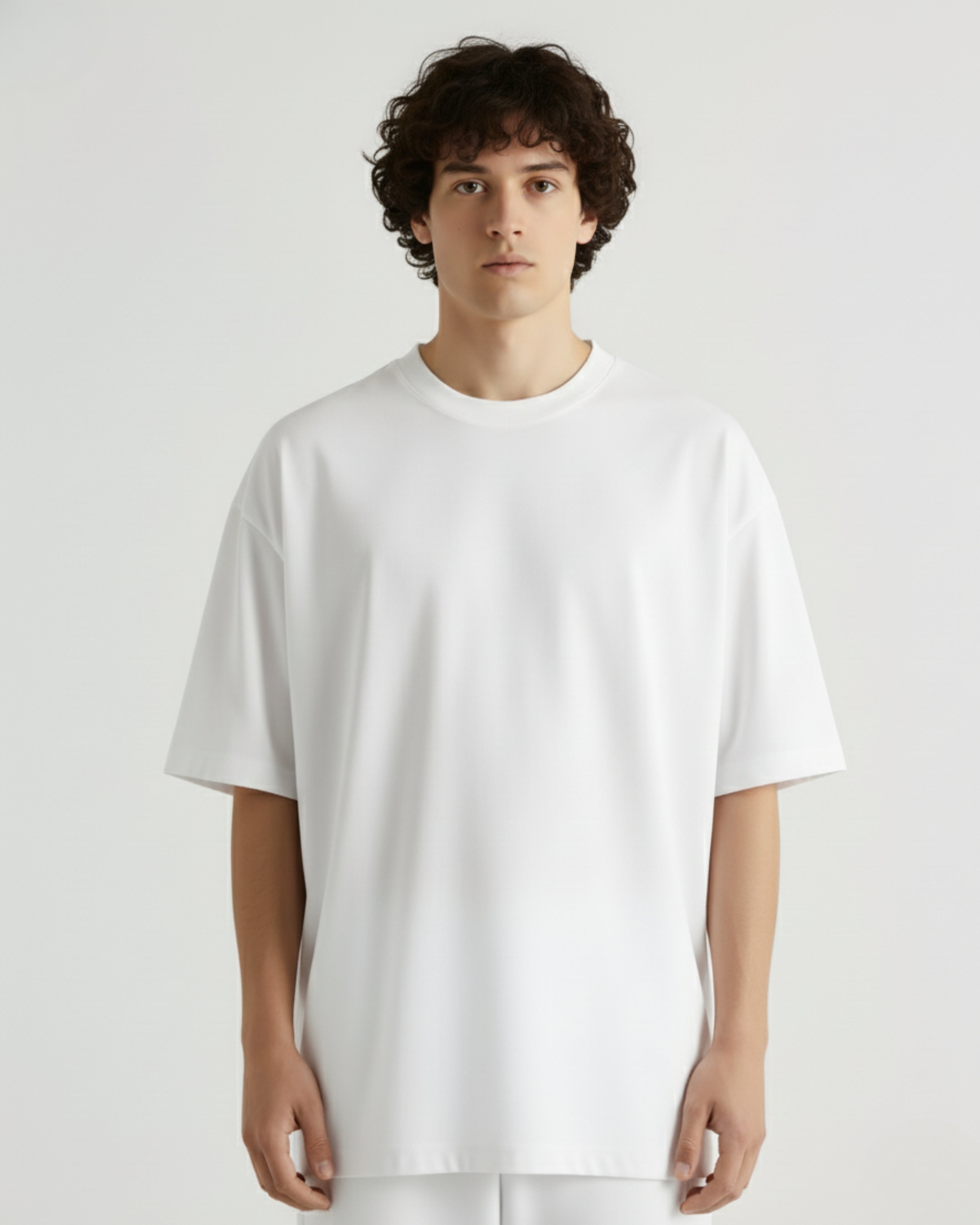 Man wearing a WHITE OVERSIZE TSHIRT and black pants standing against a white wall 